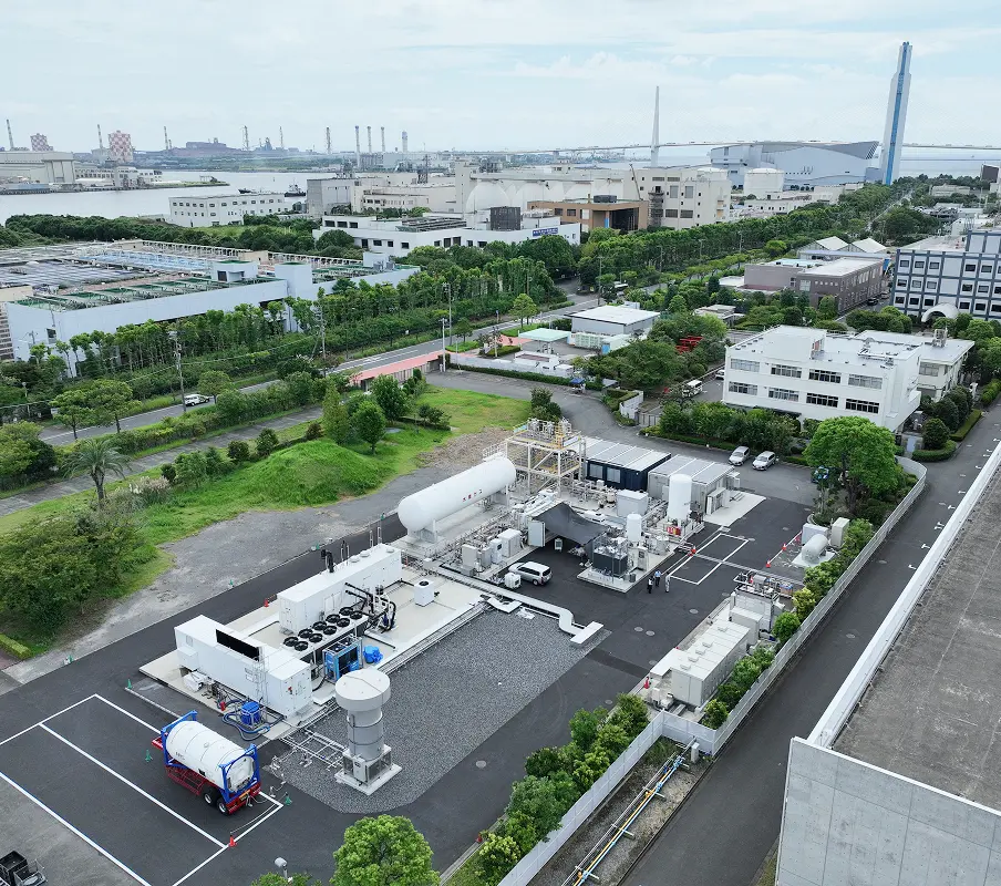清掃工場や下水道施設から回収したCO₂を活用し、e-メタンを製造する実証プラントの全景。手前には大型タンクや関連設備、奥には都市インフラが広がっている。