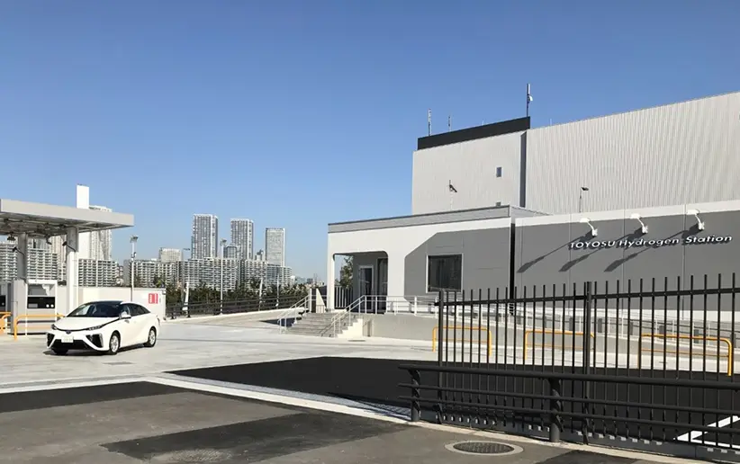 東京の豊洲にある水素ステーションの外観。手前に水素自動車が停車しており、奥には高層ビル群が見える。