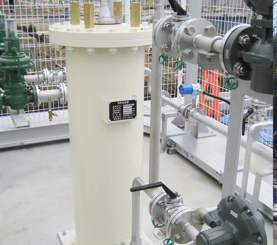 LNG関連設備の一部である縦型の白い容器とバルブ群。周囲にはフェンスと他の配管が設置されている。