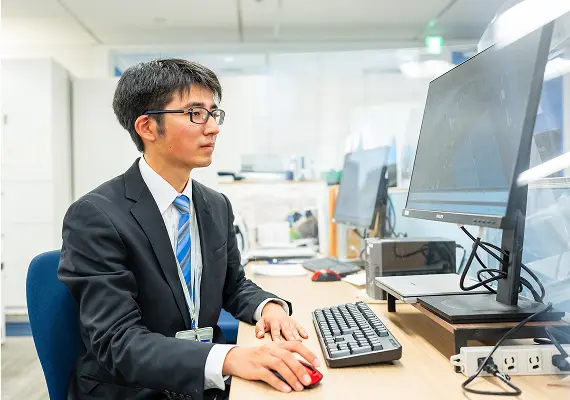 オフィスでコンピューターを使って設計・図面作成を行うスーツ姿の社員