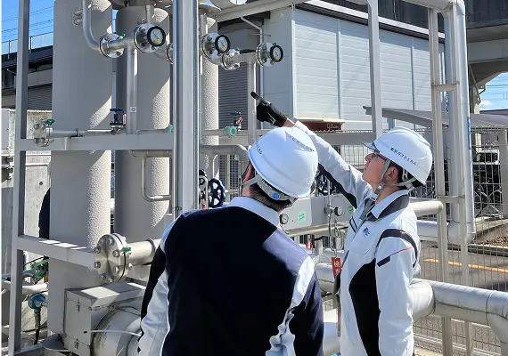 工場設備の配管やメーターを確認・点検するヘルメット着用の作業員