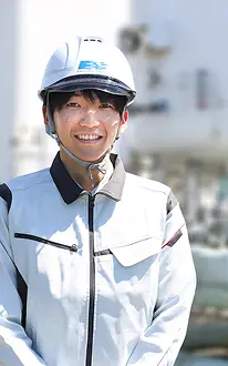 工場内でヘルメットと作業服を着用し、笑顔で立つ男性社員