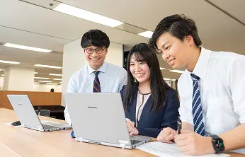 オフィスでノートパソコンを囲み、笑顔で会話する男女社員3人