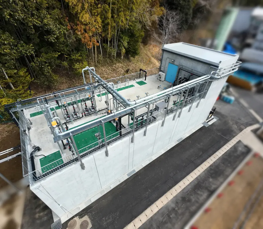 山林に隣接する工場敷地内に設置された排水処理設備の全景。配管や制御装置が屋外に設置されている様子が見える。